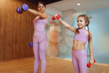 Mother and daughter doing exercise with dumbbells in gym, fitness workout. Mom and little girl in sportswear, joint training in sport club