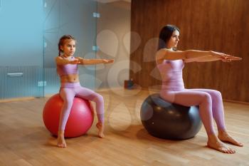Mother and daughter in gym, pilates with balls, yoga workout. Mom and little girl in sportswear, woman with kid on joint training in sport club