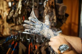Man choosing gloves for hunters on showcase in gun shop. Euqipment and rifles on stand in weapon store, hunting and sport shooting hobby