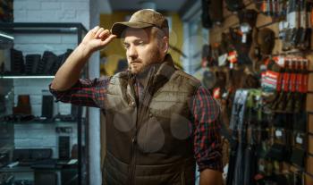 Man in cap, gun shop interior on background. Euqipment and rifles on stand in weapon store, hunting and sport shooting hobby