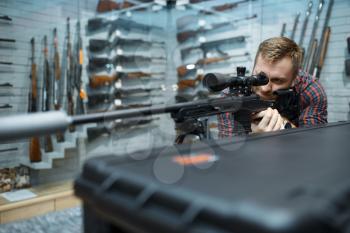 Man aims with sniper rifle in gun shop. Euqipment for hunters on stand in weapon store, hunting and sport shooting hobby
