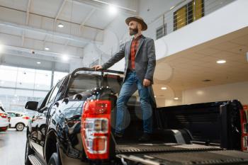 Man standing in the back of new pickup truck in car dealership. Customer in vehicle showroom, male person buying transport, auto dealer business