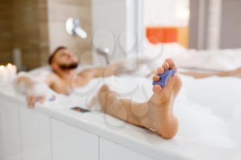 Man lying in bath with foam in the morning. Male person relax in bathroom, skin and body treatments procedures