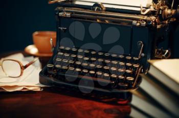 Vintage typewriter on wooden table in home office, nobody. Writer workplace in retro style, cup of coffee and glasses