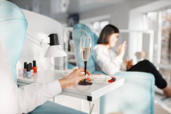 Two women with champagne in beauty salon. Professional beautician service, female customers, toenail and fingernail care in spa