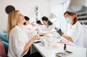 Group of women relax on manicure procedure in beauty salon. Professional beautician and female customers, nail care in spa, fingernail treatment