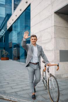 Businessman cyclist in suit in downtown, glass building on background. Business person riding on eco transport on city street