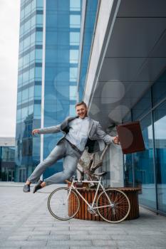Happy businessman with bicycle at the office building in downtown. Business person riding on eco transport on city street, urban style