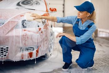 Female washer with sponge wipes the automobile headlights, car wash. Woman cleans vehicle, carwash station, car-wash business