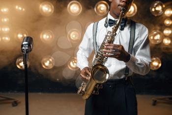 Black jazz performer plays the saxophone on the stage with spotlights. Black jazzman preforming on the scene