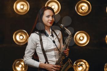 Female saxophonist plays the saxophone on the stage with spotlights. Jazz performer playing on the scene