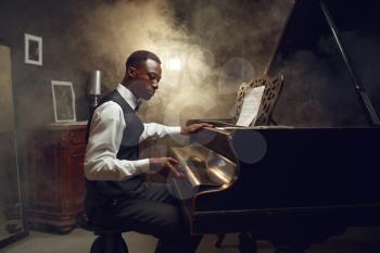 Ebony pianist, jazz performer on the stage with spotlights on background. Negro musician poses at musical instrument before the concert