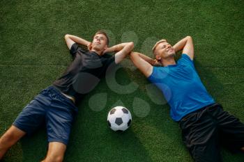 Two male soccer players lying on the grass on the field, top view. Footballer on outdoor stadium, workout before game, football training