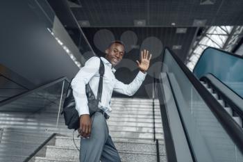Happy ebony businessman going up the escalator in mall. Successful business person, black man in formal wear, shopping center