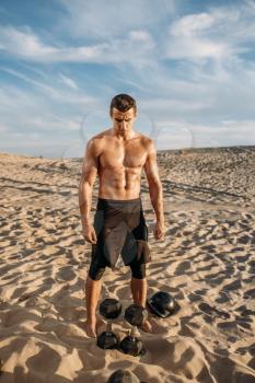 Muscular male athlete doing exercises with dumbbells in desert at sunny day. Strong motivation in sport, strength outdoor training, sportsman with weights