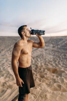 Male athlete drinks water after workout in desert at sunny day. Strong motivation in sport, strength outdoor training