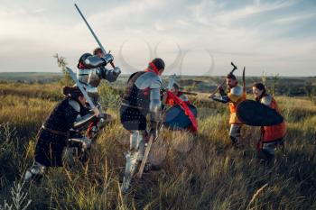 Medieval knights in armor and helmets fight with sword and axe. Armored ancient warrior in armour posing in the field