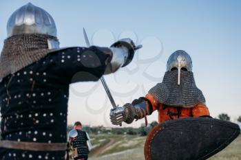 Medieval knights in armour and helmets fight with swords. Armored ancient warriors posing in the field