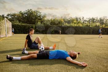 Two male soccer players resting on the grass on the field. Footballers on outdoor stadium, workout before game, football training