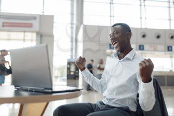 Happy black businessman sitting at laptop in car dealership. Successful business person on motor show, black man in formal wear, automobile showroom