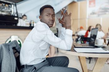 Black businessman sitting at laptop in car dealership. Successful business person on motor show, black man in formal wear, automobile showroom