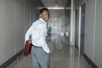 Black businessman with briefcase in office hall. Successful business person walking down the corridor, black man in formal wear