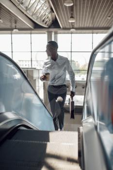 Black businessman with briefcase talking by phone on the escalator in mall. Successful business person, black man in formal wear, shopping center