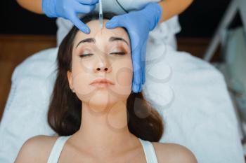 Cosmetician in gloves gives face botox injections to female patient on treatment table. Rejuvenation procedure in beautician salon. Doctor and woman, cosmetic surgery against wrinkles