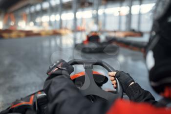 Racer in helmet driving go kart car, back view, karting auto sport indoor. Speed race on close go-kart track with tire barrier. Fast vehicle competition