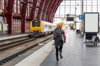 Female tourist with backpack running to the train on railway station platform, travel in Europe. Transportation by european railroads, comfortable tourism and travelling