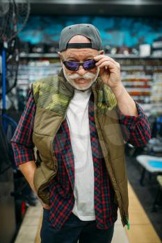 Fisherman tries on sunglasses in fishing shop. Equipment and tools for fish catching and hunting, accessory choice on showcase in store