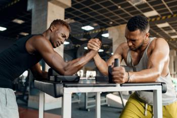 Two men fighting on their hands, arm wrestling training in gym. Fit workout in sport club, healthy lifestyle, fitness
