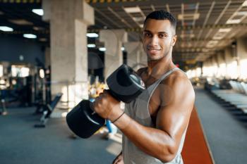 Muscular man poses with heavy dumbbell on training in gym. Fitness workout in sport club, healthy lifestyle, fit exercise