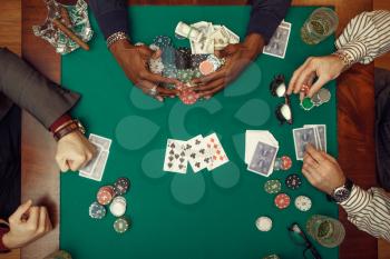 Poker players hands with cards, top view, gaming table with green cloth on background, casino. Games of chance addiction, risk, gambling house. Men leisures with whiskey and cigars