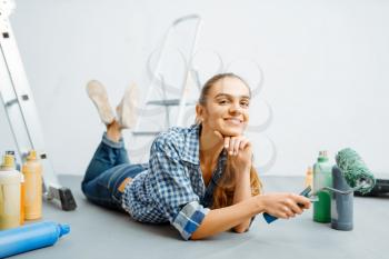 Cheerful female house painter lies on the floor. Home repair, happy woman doing appartment renovation, room decoration renovating