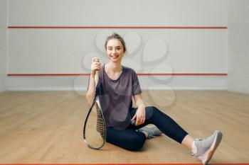 Female player with squash racket sitting on the floor. Girl on game training, active sport hobby on court