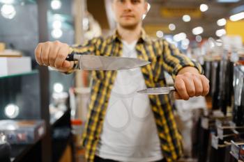 Young man holds kitchen knives in houseware store. Male person buying home goods in market, guy in kitchenware supply shop