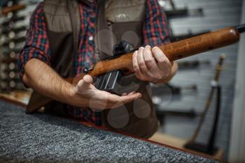 Man loads a rifle at counter in gun shop. Euqipment for hunters on stand in weapon store, hunting and sport shooting hobby