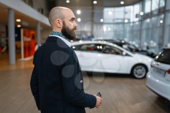 Smiling man poses in car dealership. Customer in new vehicle showroom, male person buying automobile, auto dealer business