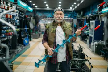 Fisherman holds a drill for winter fishing in shop. Male angler buying equipment and tools for fish catching and hunting, assortment on showcase in store
