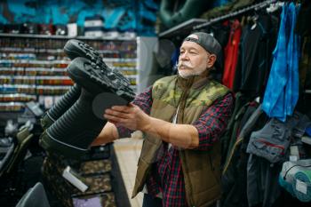 Male angler choosing rubber boots in fishing shop. Equipment and tools for fish catching and hunting, accessory choice on showcase in store