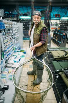 Happy angler holds net in fishing shop, hooks and baubles on background. Equipment and tools for fish catching and hunting, accessory choice on showcase in store, bait assortment