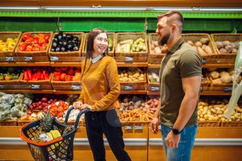 Happy couple with basket in grocery store together. Man and woman buying fruits and vegetables in market, customers shopping food