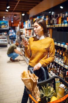 Family couple choosing alcohol products in grocery store. Man and woman with cart buying beverages in market, customers shopping food and drinks