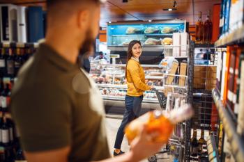 Family couple in grocery store, alcohol department. Man and woman with cart buying beverages in market, customers shopping food and drinks