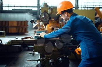 Worker in uniform and helmet works on lathe, plant. Industrial production, metalwork engineering, power machines manufacturing