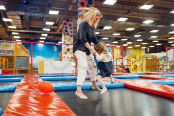 Mother and little girl jumping on a trampoline in the entertainment center. Mom and her daughter leisures on holidays, childhood happiness, happy kids on playground