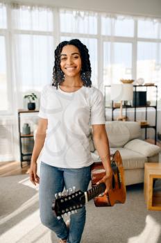 Attractive woman with guitar poses at home. Pretty lady with musical instrument relax in the room, female music lover resting