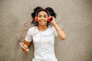 Cute woman in headphones lying on the floor and listen to music, top view. Pretty lady in earphones relax in the room, female sound lover resting