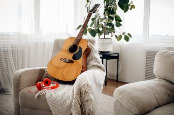Guitar and headphones on white armchair at home, nobody. Acoustic musical instrument and earphones in the room, music lovers concept